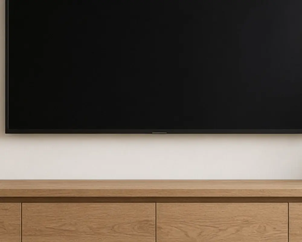A living room with a low oak media console under a wall-mounted TV, a lamp, and a plant beside it